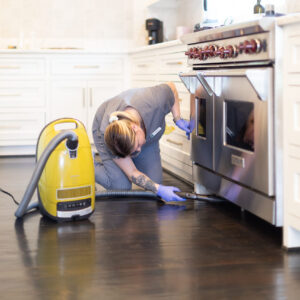 A Vella Housekeeper vacuuming below the oven to ensure every single nook and cranny is completely clean.