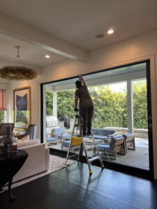 Vella professional cleaner on a ladder wiping a large interior glass wall with a microfiber cloth in Plano, Texas.