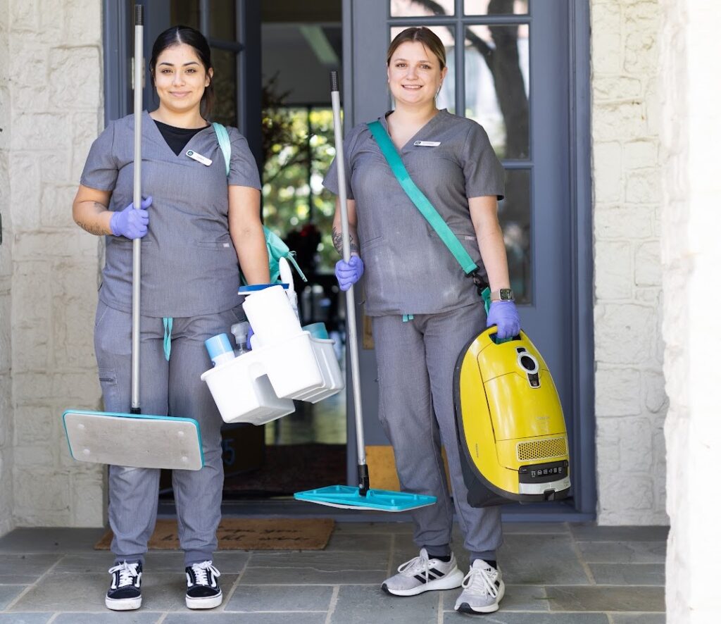 Two house cleaners in uniforms holding cleaning supplies and a vacuum, ready for house cleaning with pets.