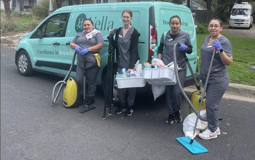 Housekeeping team standing in front of a teal van, equipped with cleaning tools including a vacuum and mop, ready for an assignment.