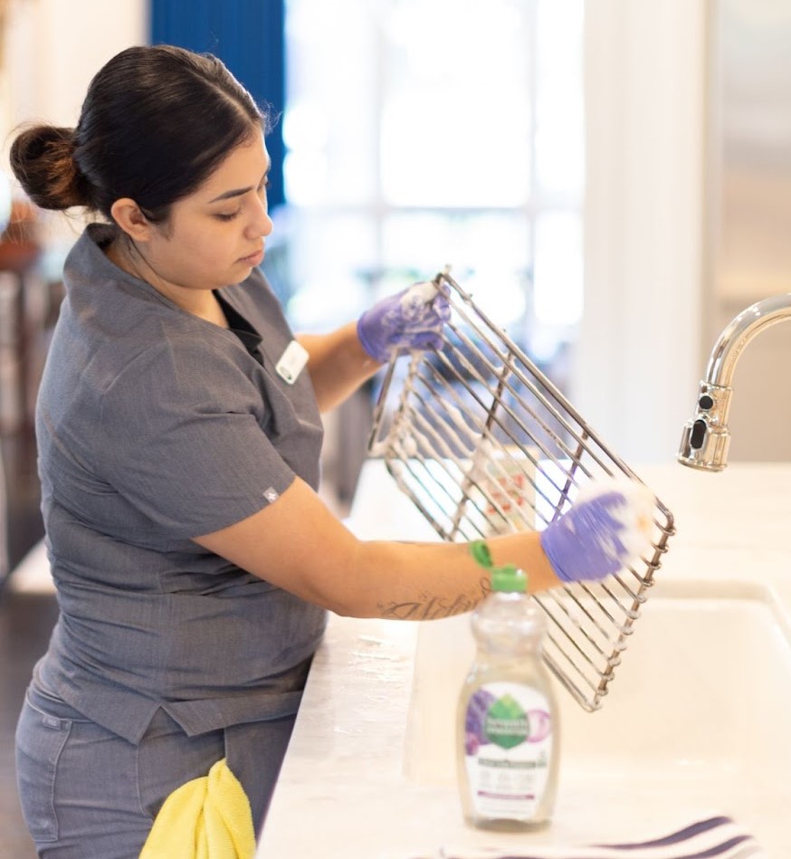 Professional cleaner using a vacuum to clean under a stove in a modern kitchen.