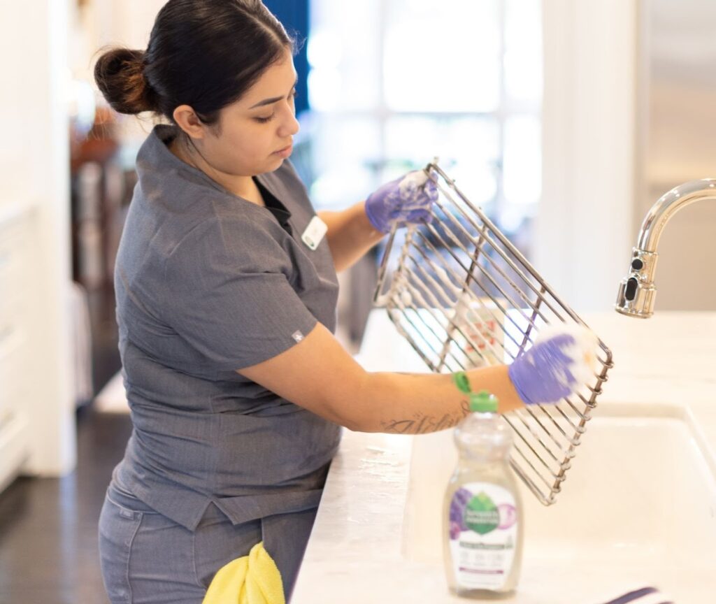 "Professional cleaner scrubbing a kitchen rack over the sink, demonstrating effective techniques for cleaning your kitchen with eco-friendly products."