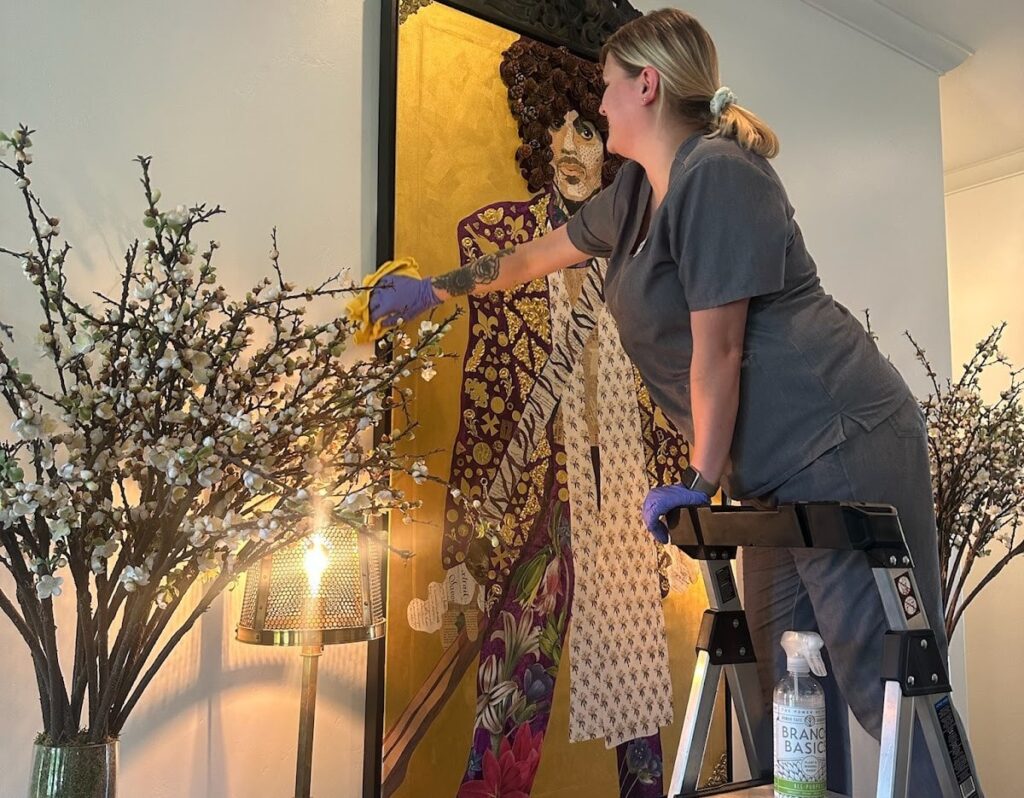 A cleaner standing on a step stool dusts intricate decor, highlighting the attention to detail needed when you deep clean your kitchen and adjacent spaces.