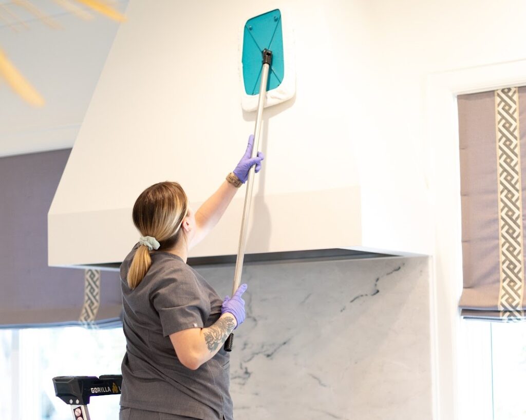 A cleaning professional using a  tool to wipe a kitchen hood, highlighting the need to clean your kitchen hood effectively.