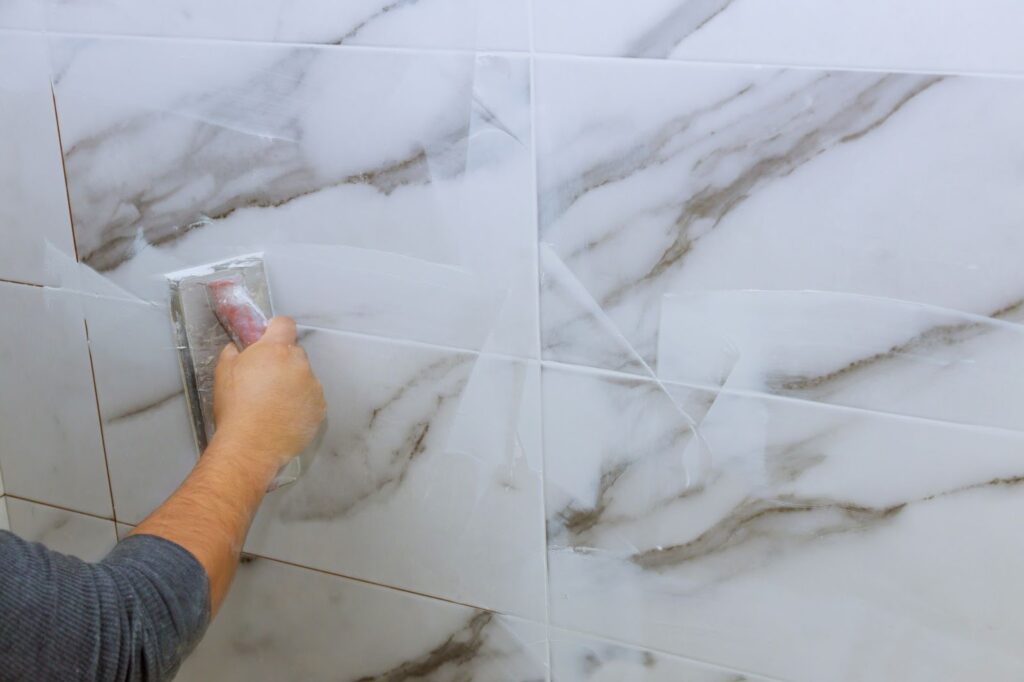 A hand holding a grout float tool against a background of marble-patterned tiles.