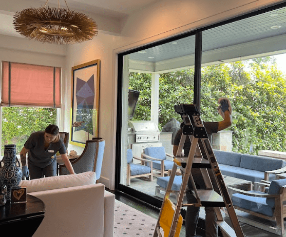 Two professional cleaners performing regular home cleaning, tidying up an elegant living room and ensuring sparkling clean glass doors.