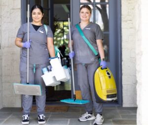 Vella cleaning staff standing with non-toxic cleaners and a vacuum in front of a house in Austin.