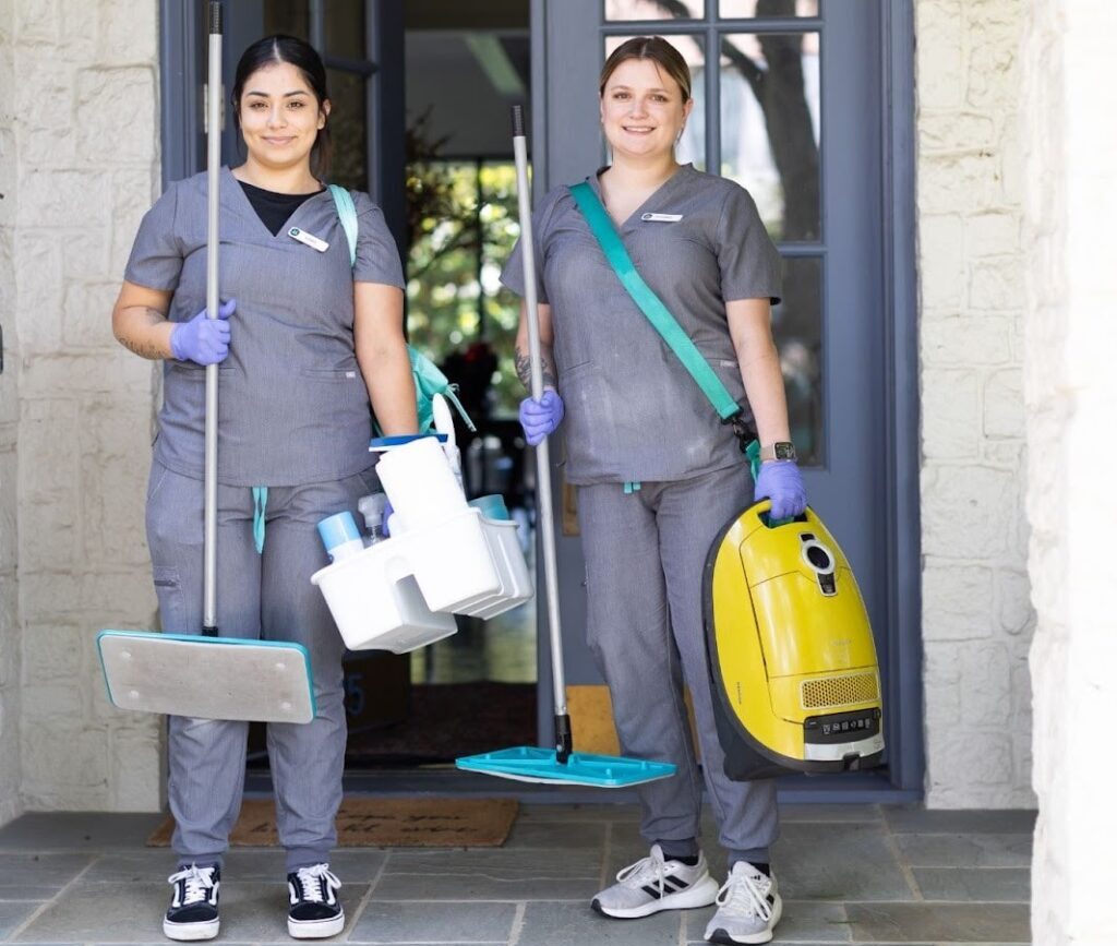 Vella cleaning staff standing with non-toxic cleaners and a vacuum in front of a house in Austin.