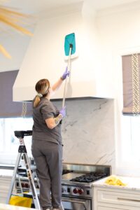 Vella staff cleaning a kitchen chimney using a Shy-mop while standing on a ladder in a Plano, Texas home.
