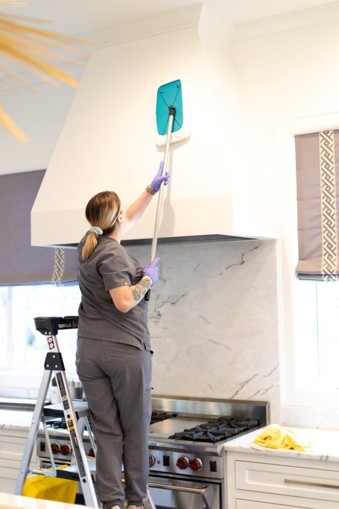 Vella staff cleaning a kitchen chimney using a Shy-mop while standing on a ladder in a Plano, Texas home.