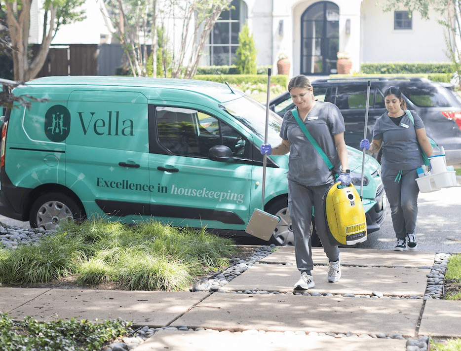 Two cleaners with equipment walk from a branded "Vella" van, offering deep cleaning services in Austin.
