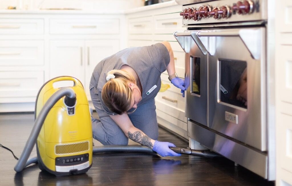 A professional cleaner vacuuming under a microwave, demonstrating how to clean your microwave effectively and maintain a tidy kitchen