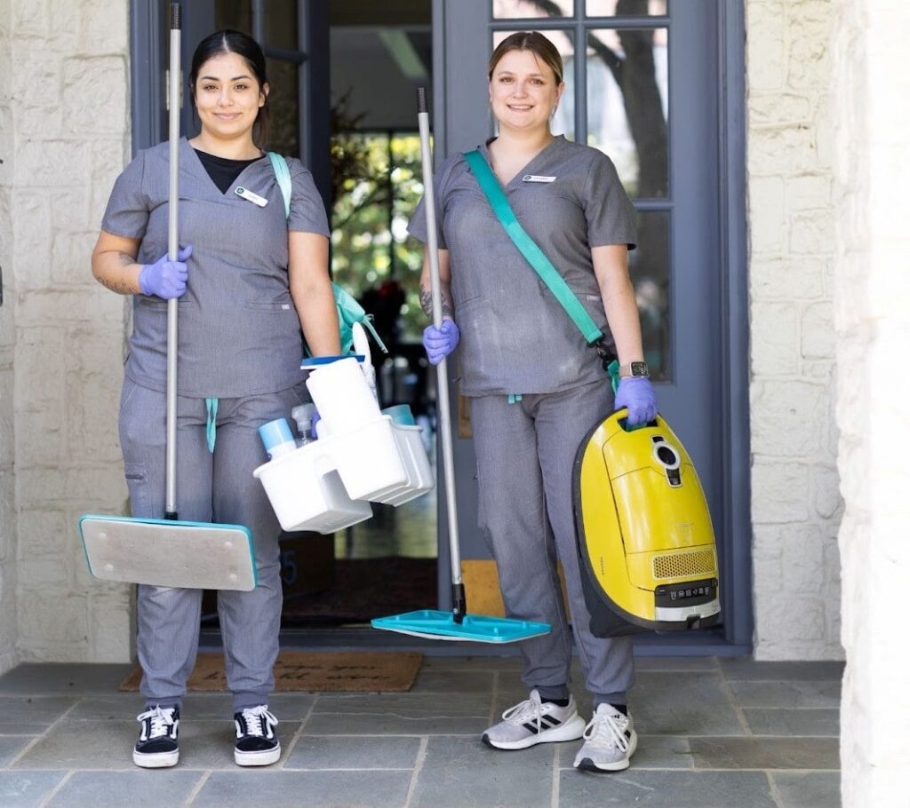 Two smiling Vella housekeepers standing in front of an Austin home they just cleaned.
