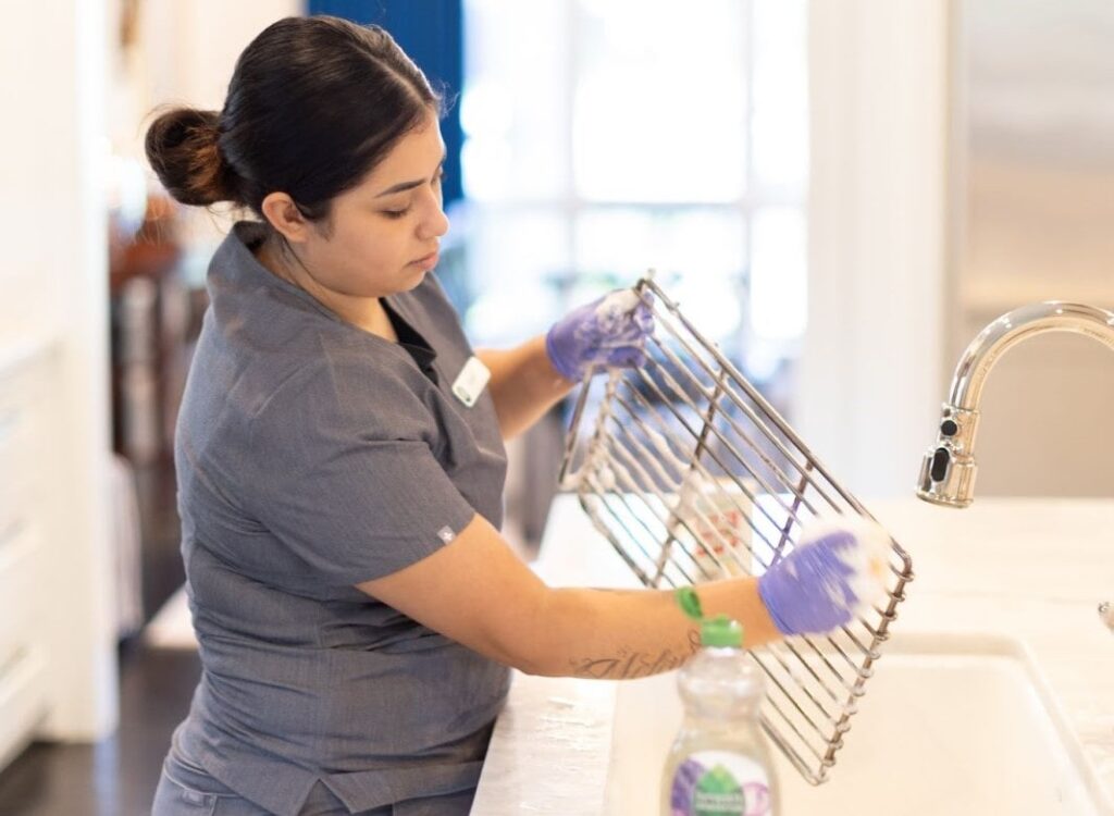 A cleaner washing a microwave rack with soapy water, showcasing the process to clean your microwave accessories thoroughly.