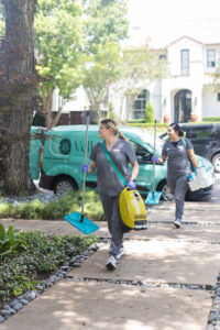 Two cleaning staff from Vella walk from their van with a vacuum cleaning, cleaning products, and a shy mop.