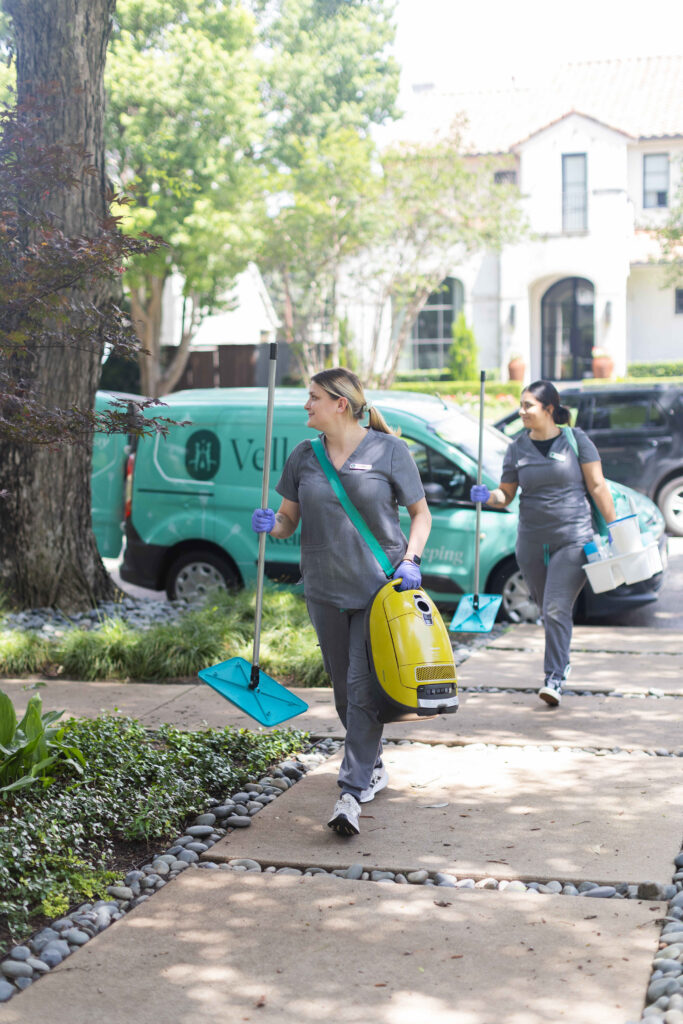 Two Vella cleaners entering an Austin home with eco-friendly supplies for a comprehensive spring cleaning service.
