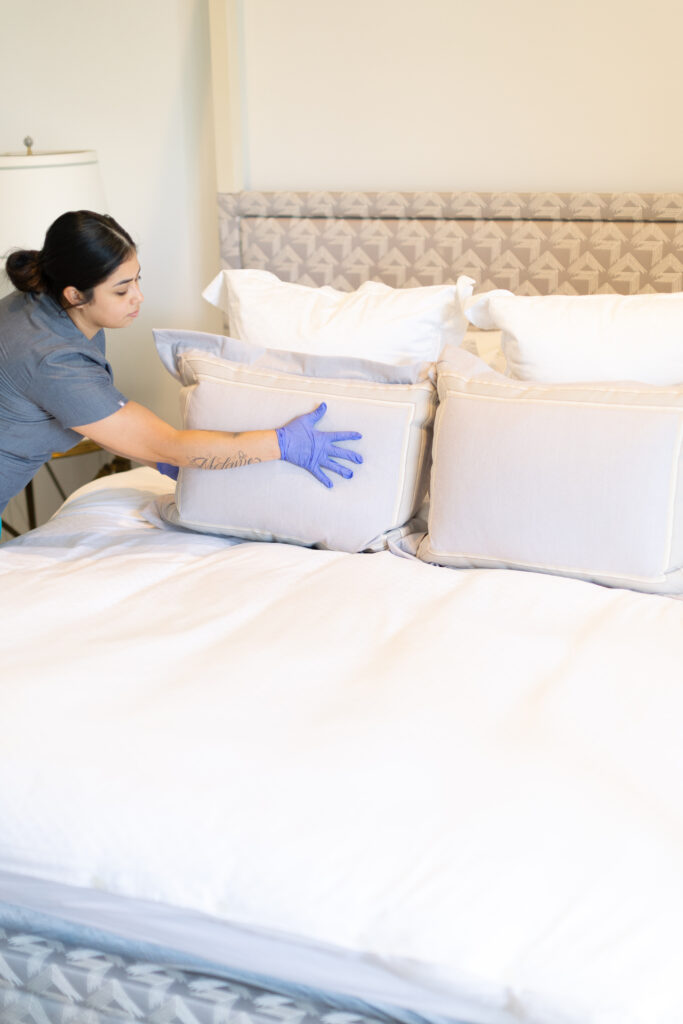 Vella's housekeeper neatly arranging pillows on a luxury hotel bed, ensuring cleanliness, comfort, and a polished look.
