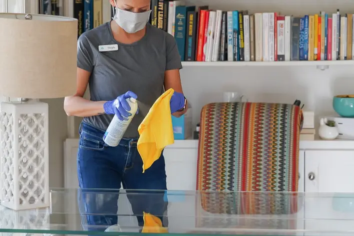 Vella team member wiping a glass table with non-toxic cleaner and microfiber cloth during spring cleaning in Austin.