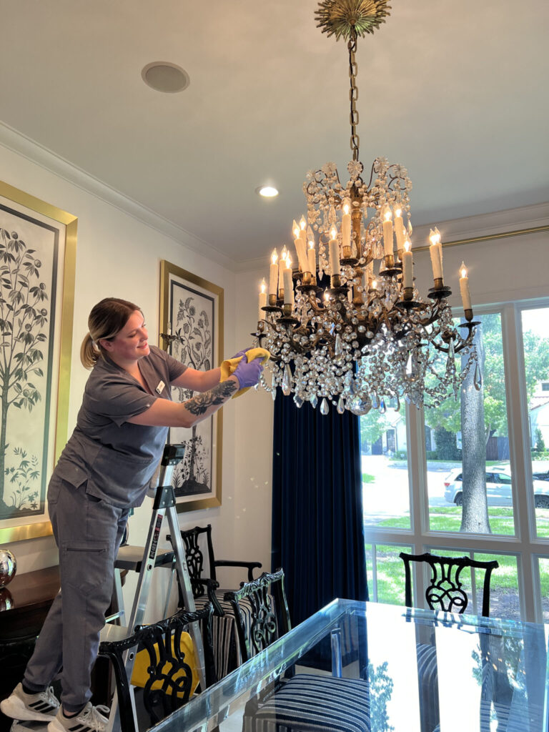 Vella staff cleaning chandelier while standing on ladder inside a Plano, Texas home.