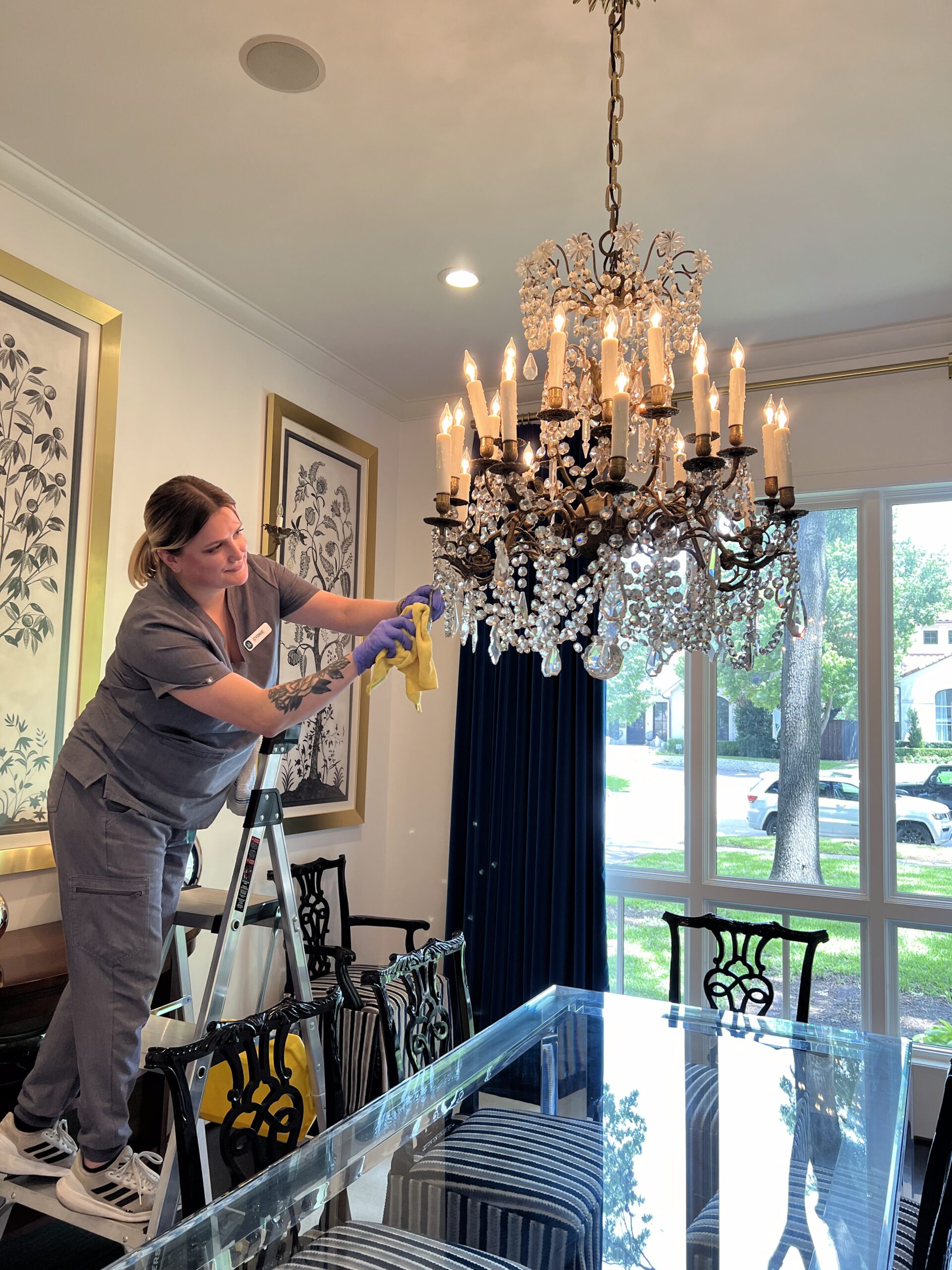 A Vella’s cleaning staff member on a ladder cleaning the chandelier in a home in Austin.