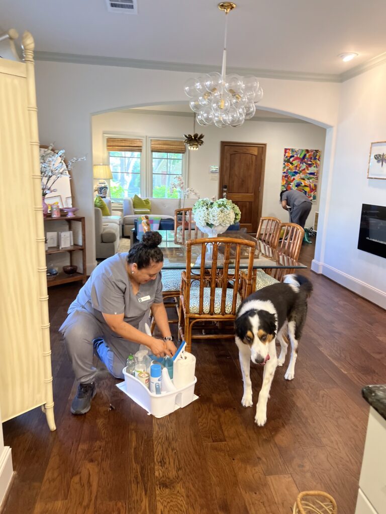 A Vella cleaning staff in an Austin home using eco-friendly cleaning products, with a pet dog nearby.
