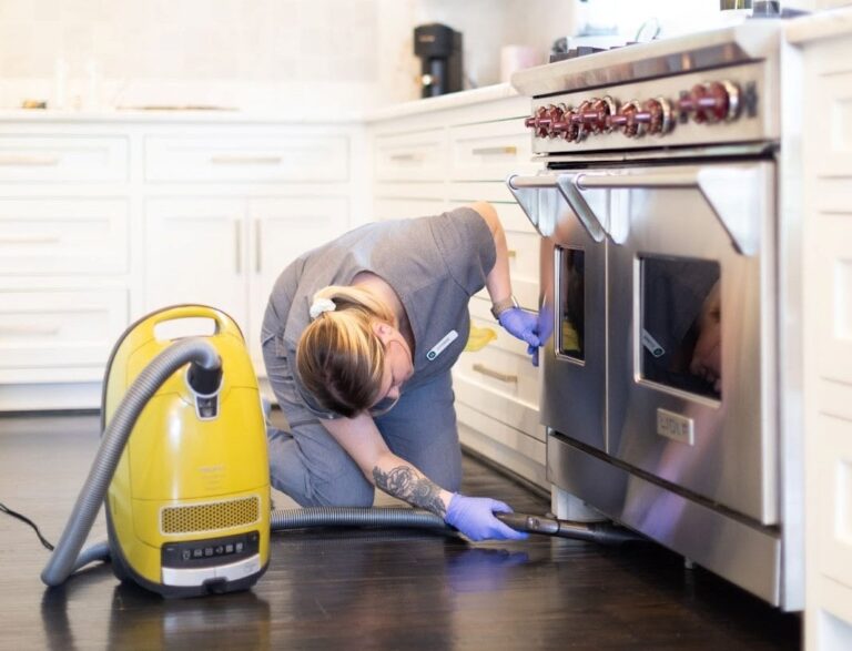 Vella staff vacuuming dirt from under stove counter in a Fort Worth home.