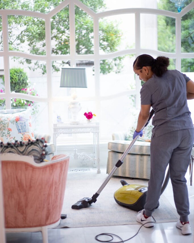Vella staff member vacuuming a living room floor in a Dallas home before guest arrival.