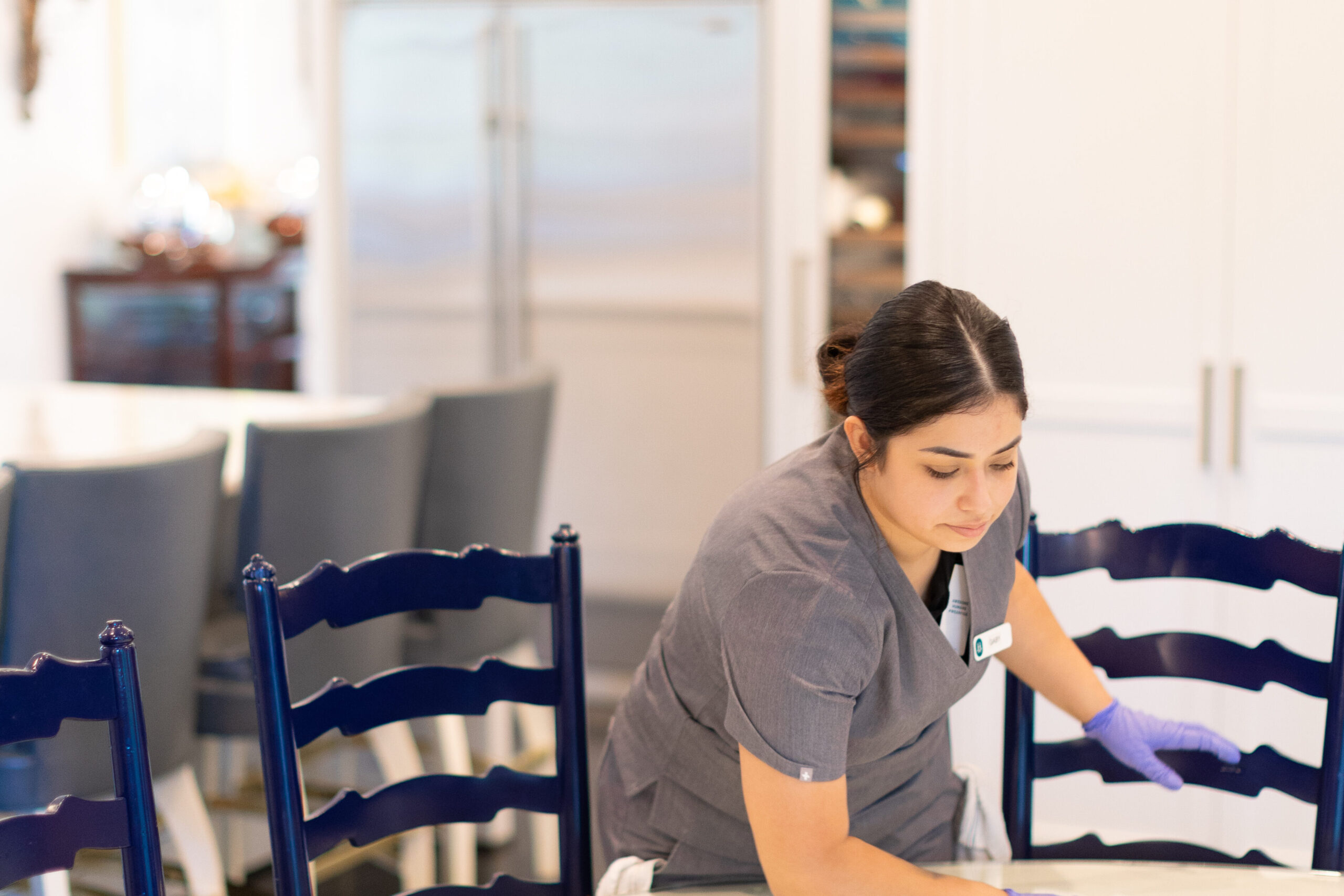 Vella’s cleaning staff wiping wooden dining set with nontoxic cleaner and microfiber cloth inside a Dallas home.