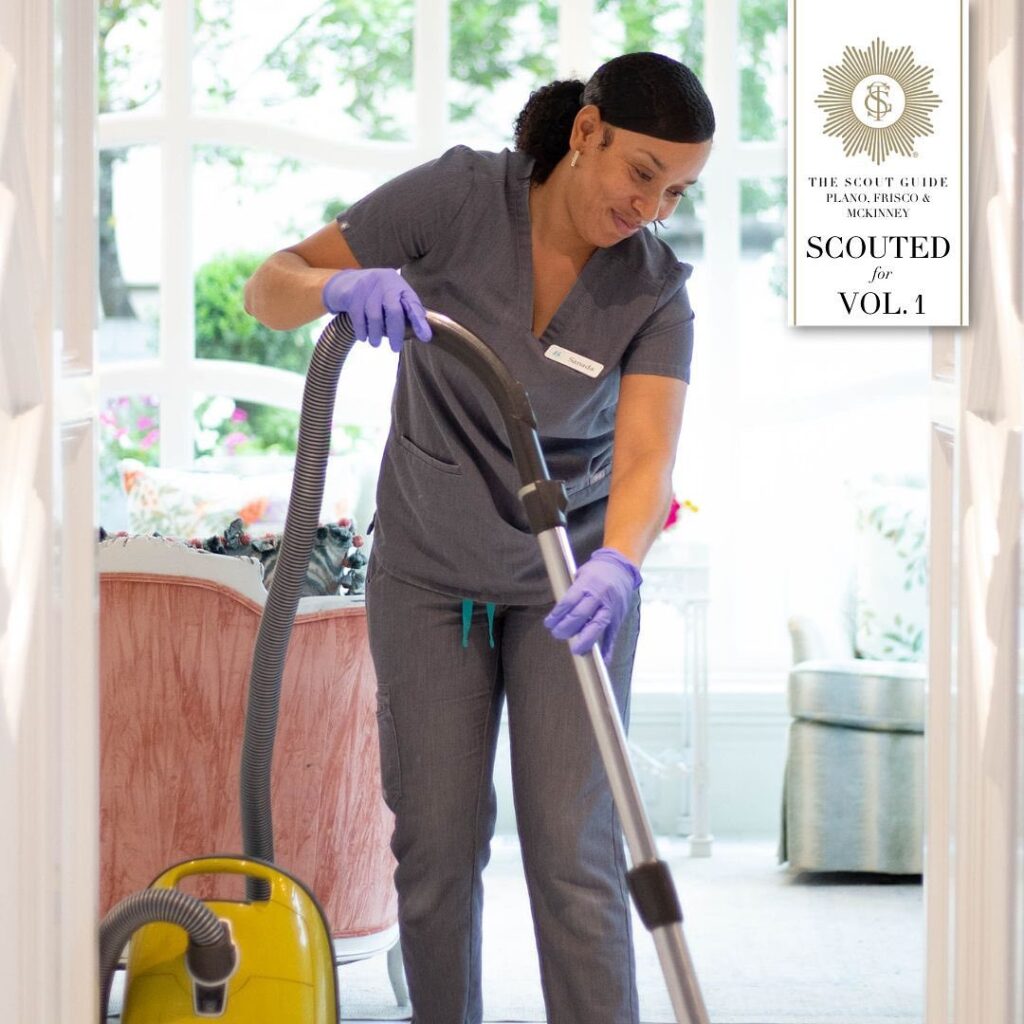 A Vella cleaning professional vacuuming a house with a smile.
