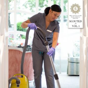 A Vella cleaning professional vacuuming a house with a smile.
