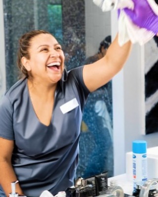 A Vella professional cleaning a glass mirror with Sprayway cleaner for seasonal home maintenance.