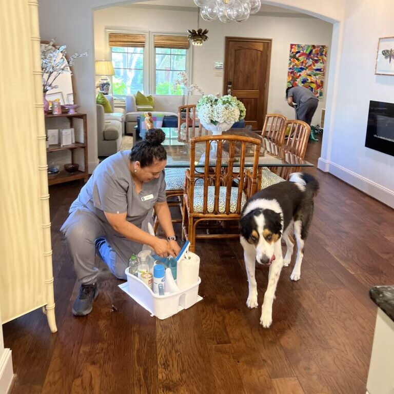 Vella cleaning staff in Austin standing with eco-friendly cleaning products beside a family pet dog.