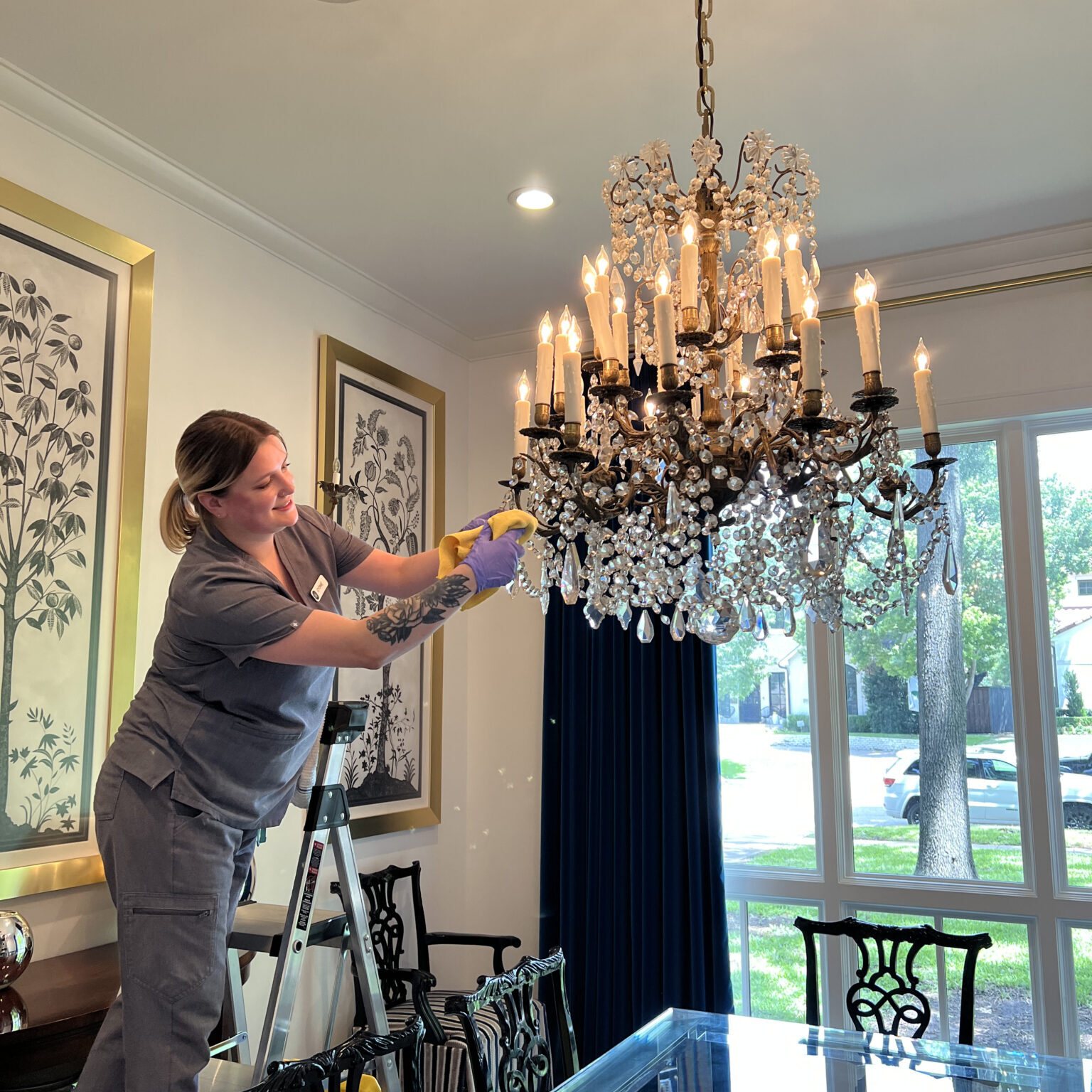 A professional cleaner from Vella carefully cleaning a chandelier inside a modern Austin home to improve indoor air quality.