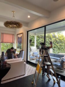 Two cleaning staff members are tidying a modern living room and washing large glass patio doors.