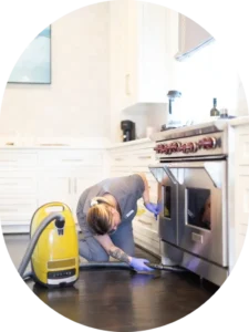 A Vella cleaning professional vacuuming under a stove during a detailed move-in clean in an Austin home.