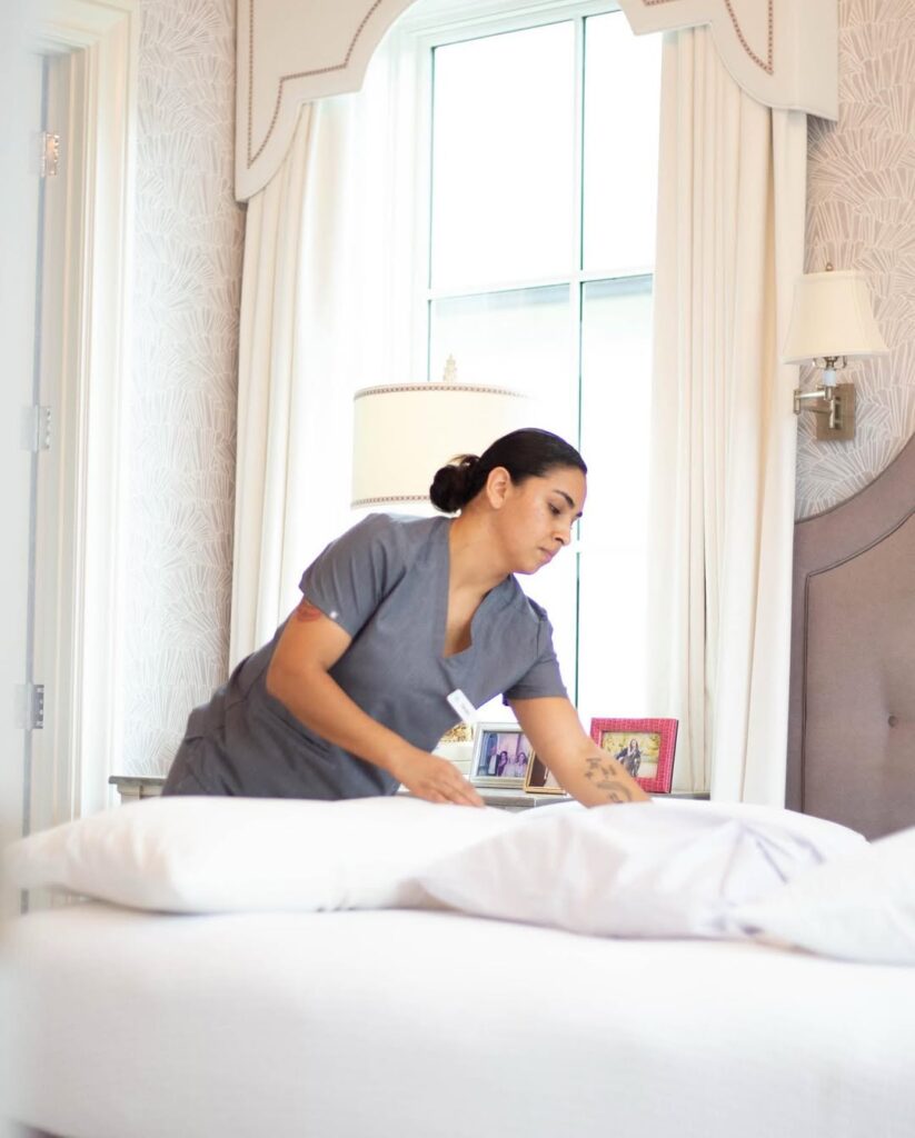 Vella cleaner making a bed and arranging pillows in a bright bedroom