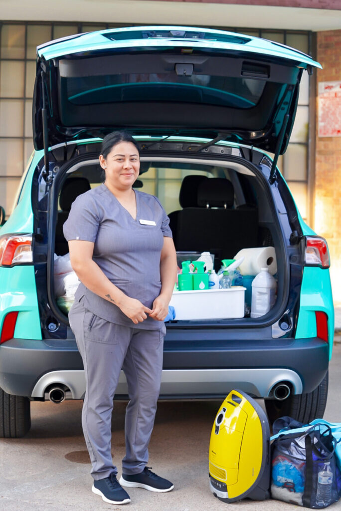 Vella cleaning professional standing in front of a service van in Austin, holding cleaning tools and supplies.