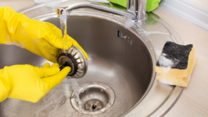 Professional cleaner wearing gloves cleaning a garbage disposal under running water to maintain a hygienic kitchen sink.