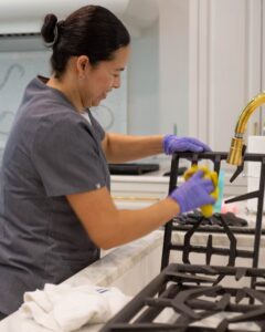 Professional Vella cleaner scrubbing a stove grate in a modern kitchen during a residential deep cleaning service.